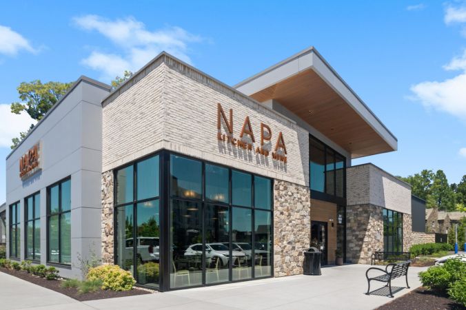 Modern building with large windows and “NAPA Kitchen and Wine” sign, under a blue sky with a few clouds.