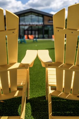Two yellow Adirondack chairs on green grass facing a modern building under a partly cloudy sky.