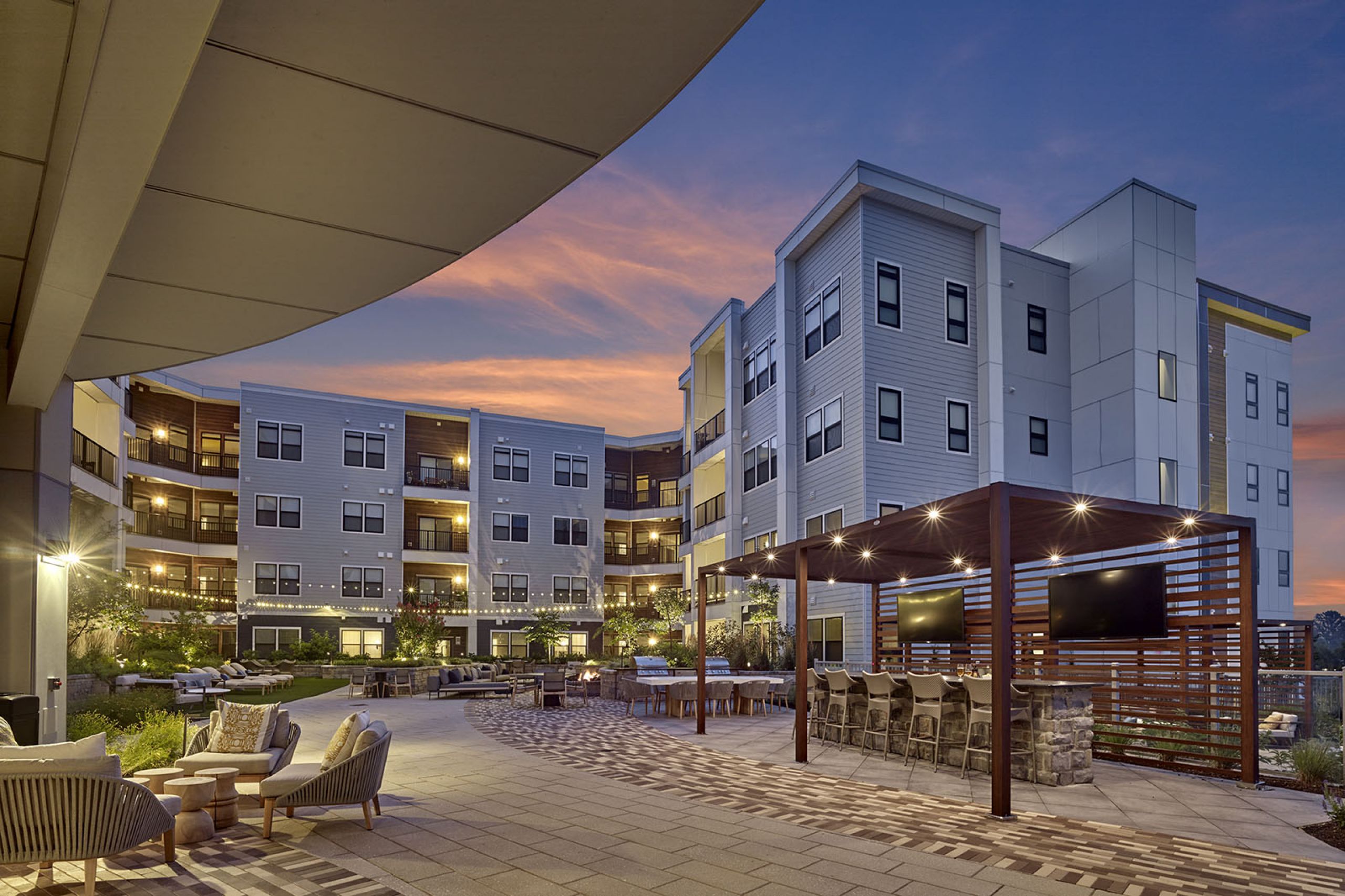 Modern apartment complex at sunset with outdoor seating, string lights, and a covered lounge area.