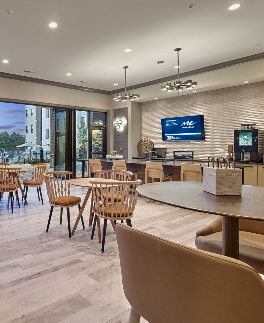 Modern hotel lounge with wooden chairs, open sliding doors, TV, and a coffee station, warmly lit.