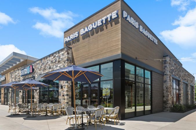 Outdoor seating at a Paris Baguette bakery café with blue umbrellas and sunny weather.