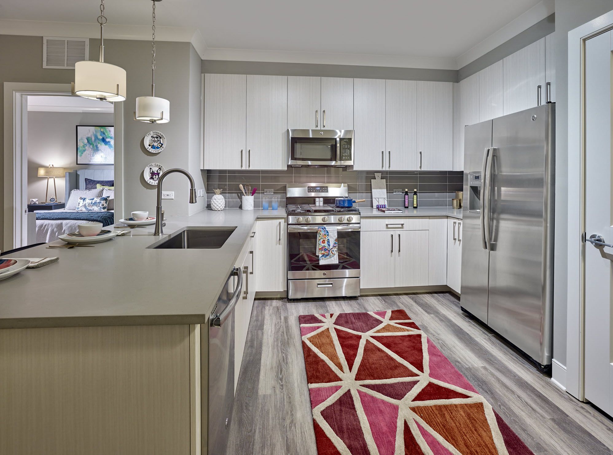 Modern kitchen with stainless steel appliances, white cabinets, and a red geometric rug on wood floors.