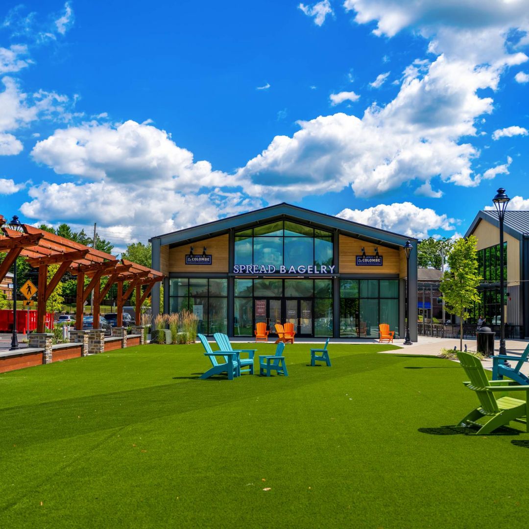Outdoor seating area with colorful chairs on green turf, in front of a modern bakery building under a blue sky.