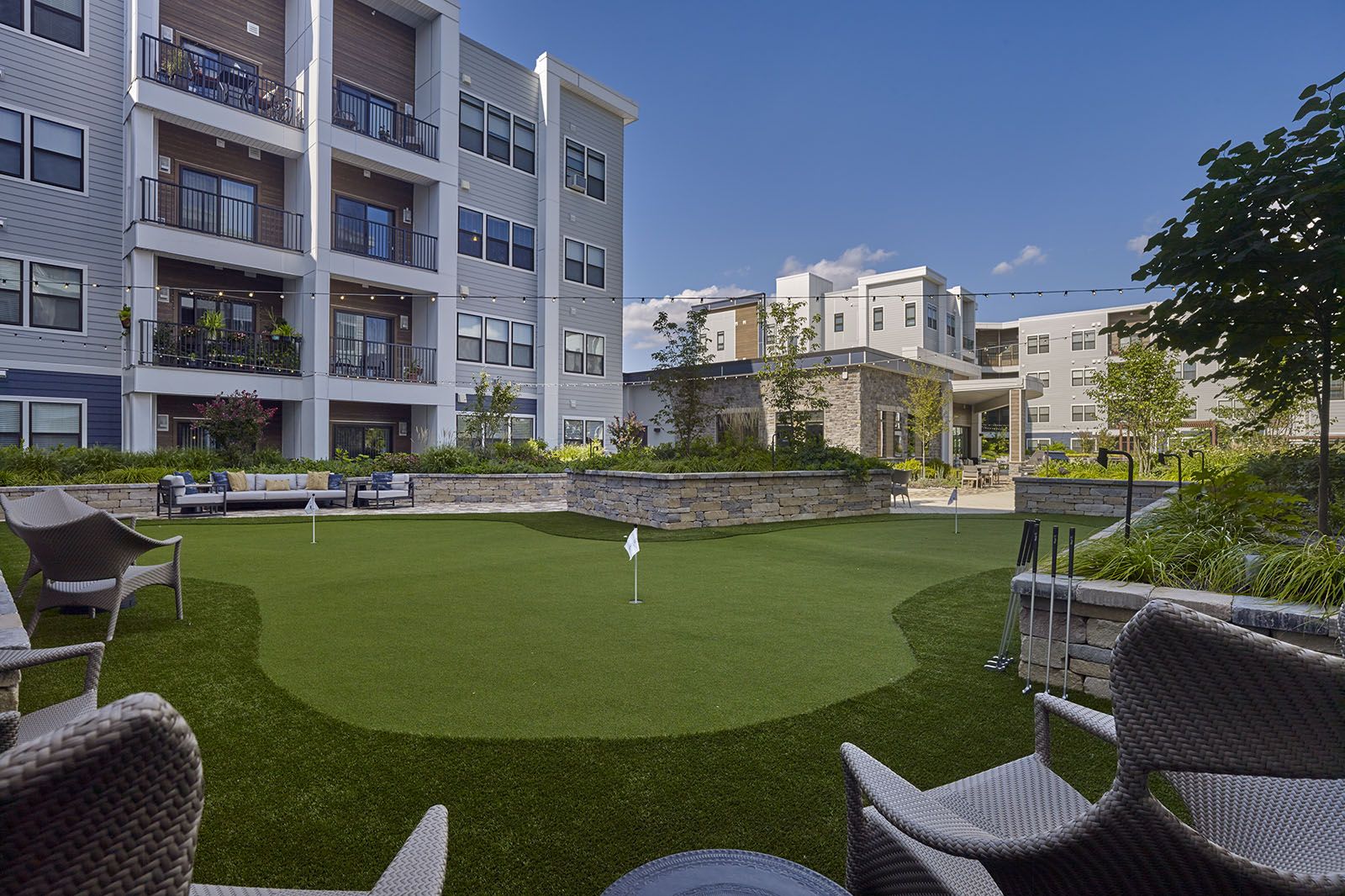 Apartment courtyard with putting green, lounge chairs, and surrounding modern buildings under a blue sky.