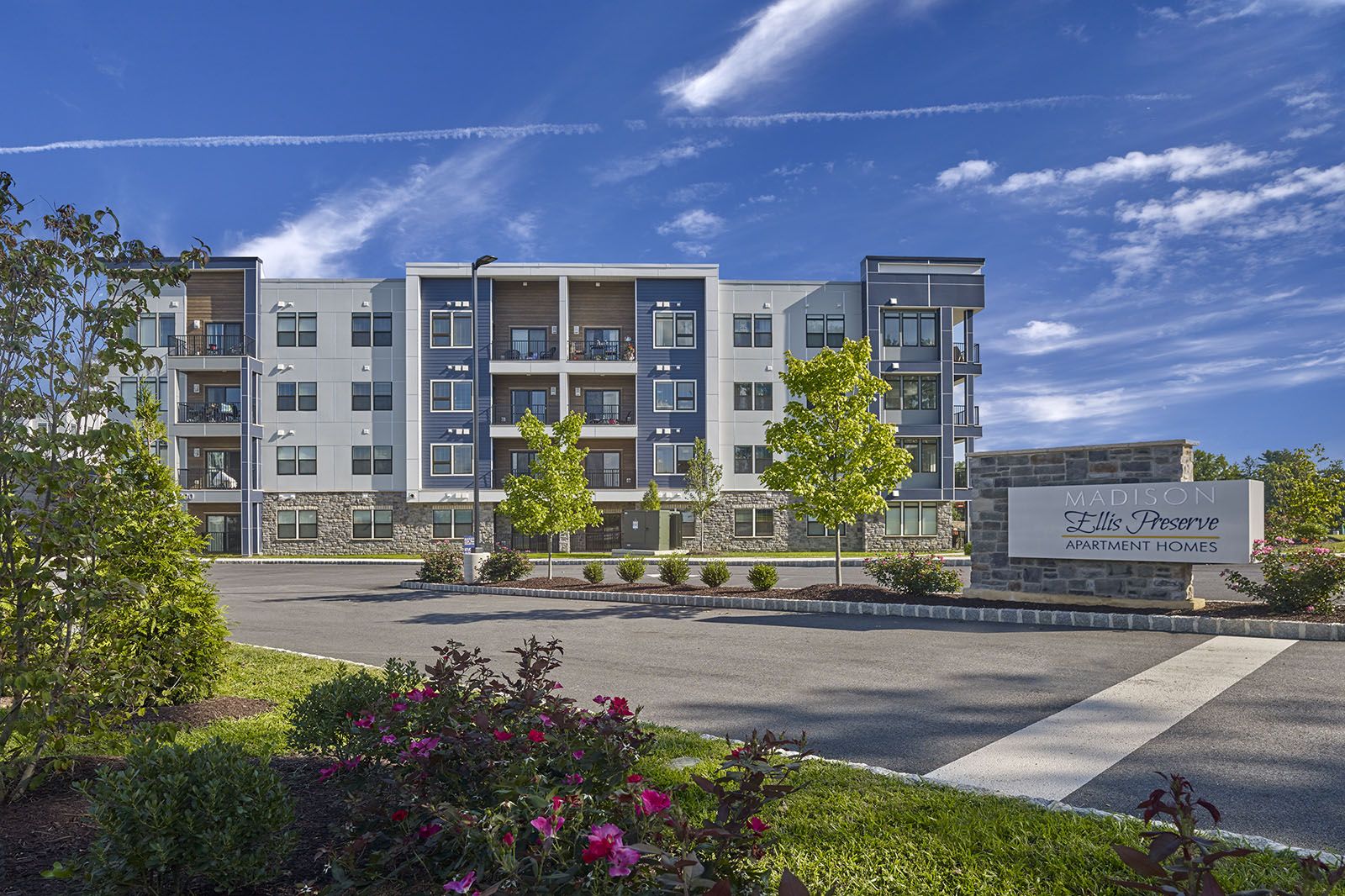 Modern four-story apartment building with balconies, landscaped grounds, and a sign reading "Madison Hills Preserve.