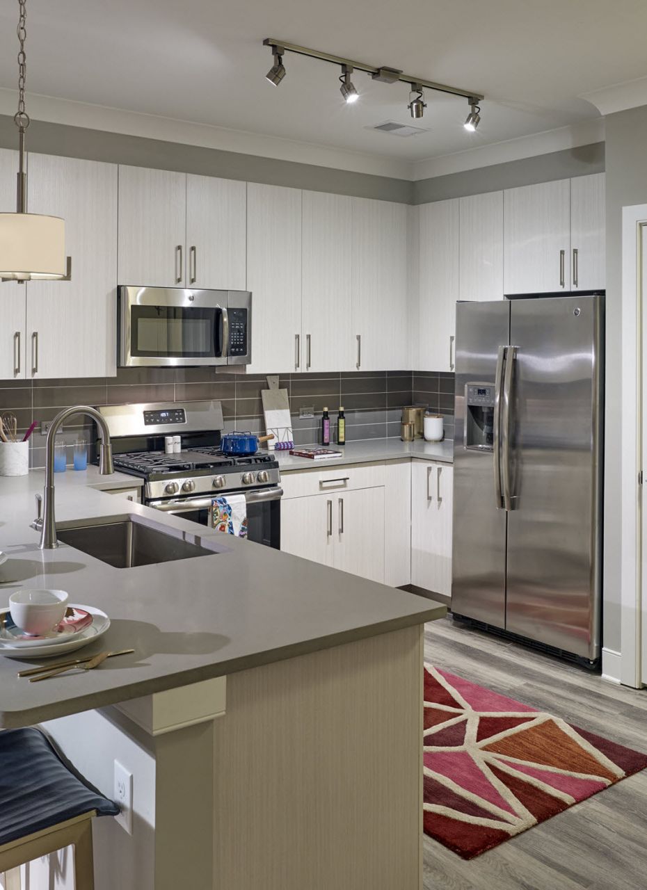 Modern kitchen with stainless steel appliances, bar seating, and a red geometric rug on wood floors.