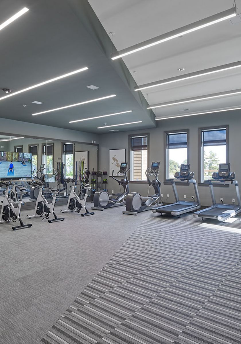 Modern gym with cardio machines, free weights, benches, mirrors, and fitness accessories in a bright, spacious room.