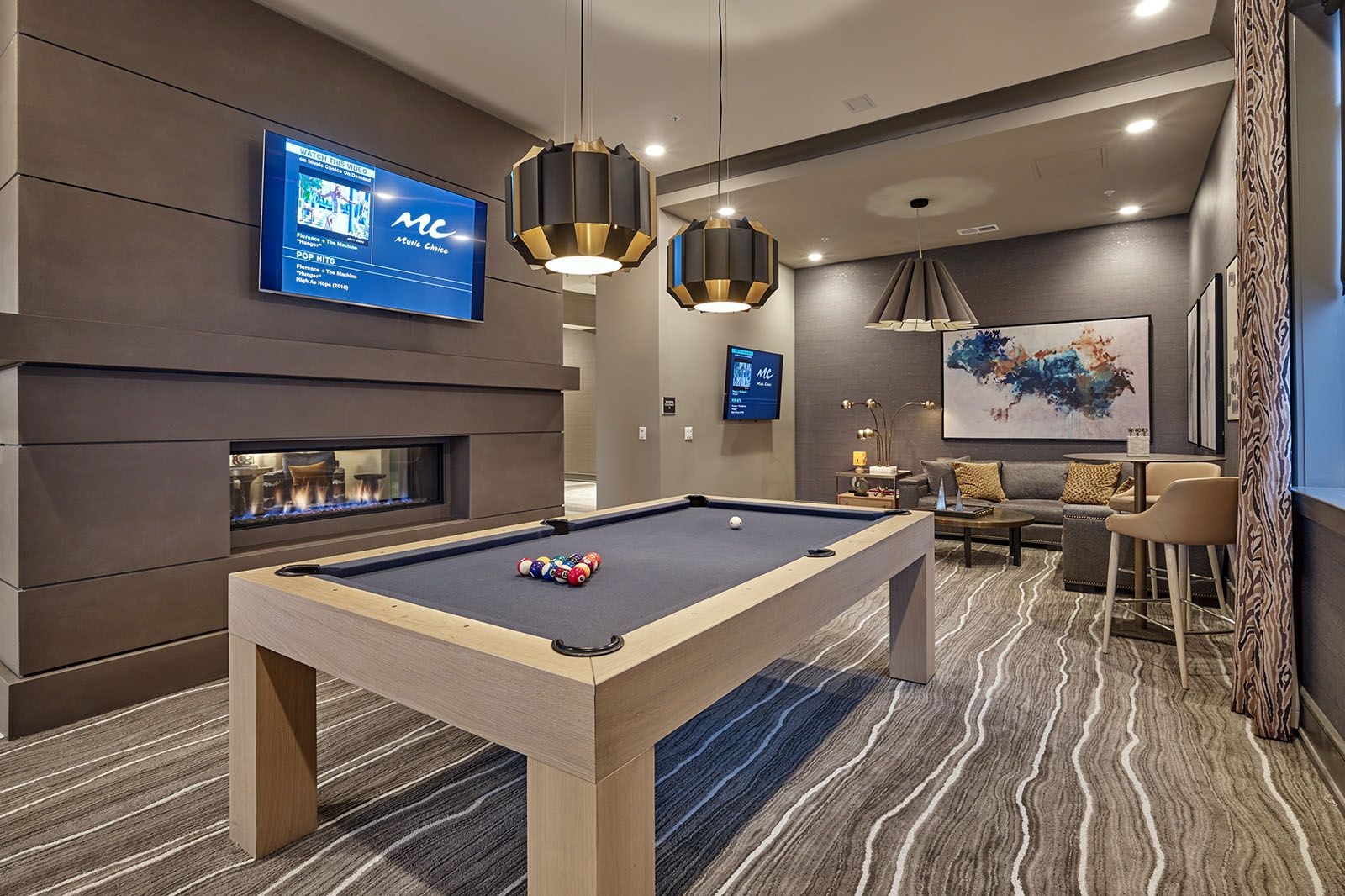 Modern game room with a pool table, fireplace, TVs, and stylish seating area with abstract wall art.