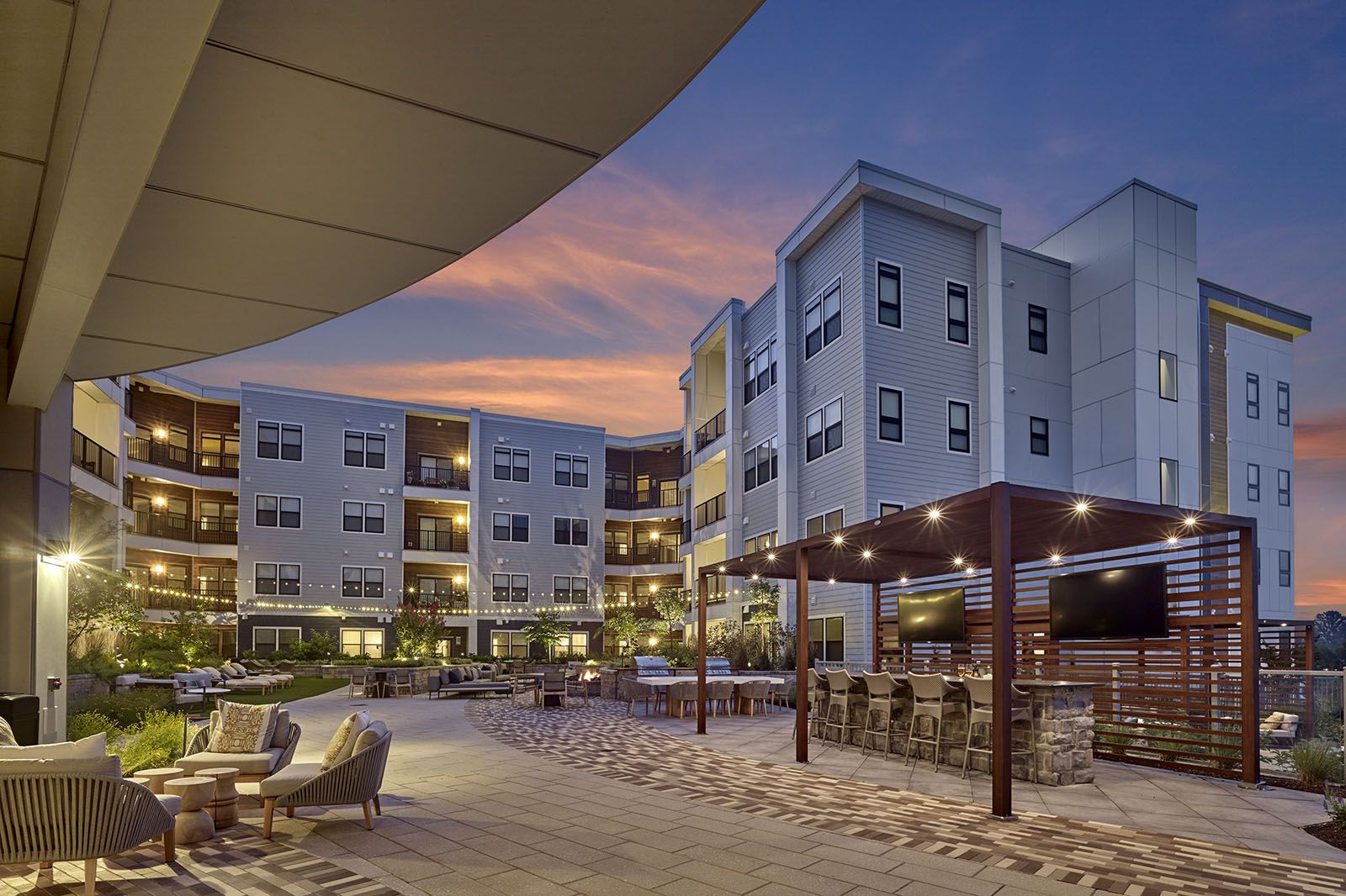 Modern apartment complex at sunset with outdoor seating, string lights, and a covered lounge area.